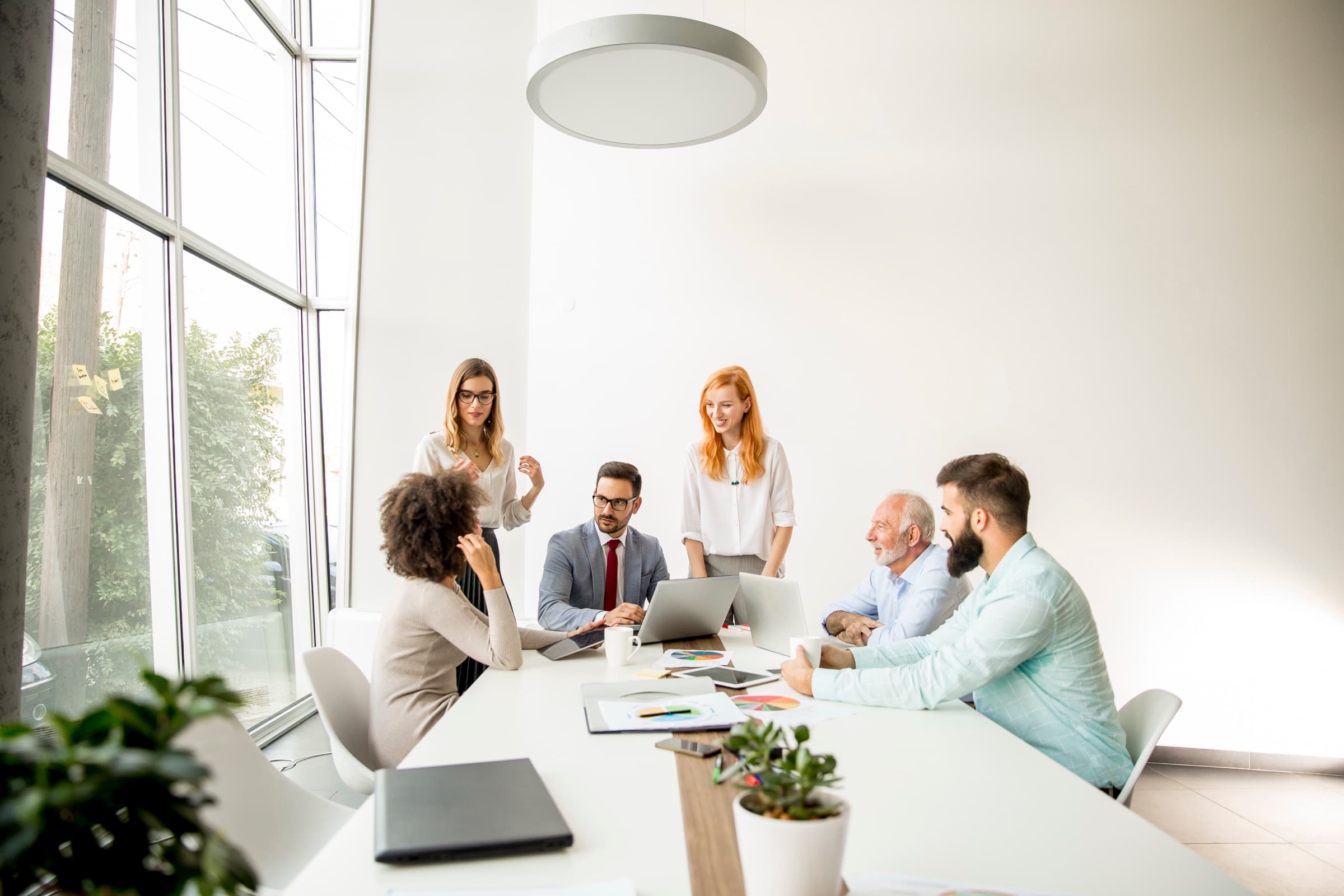 A team working together around a long table covered in papers, in a bright office