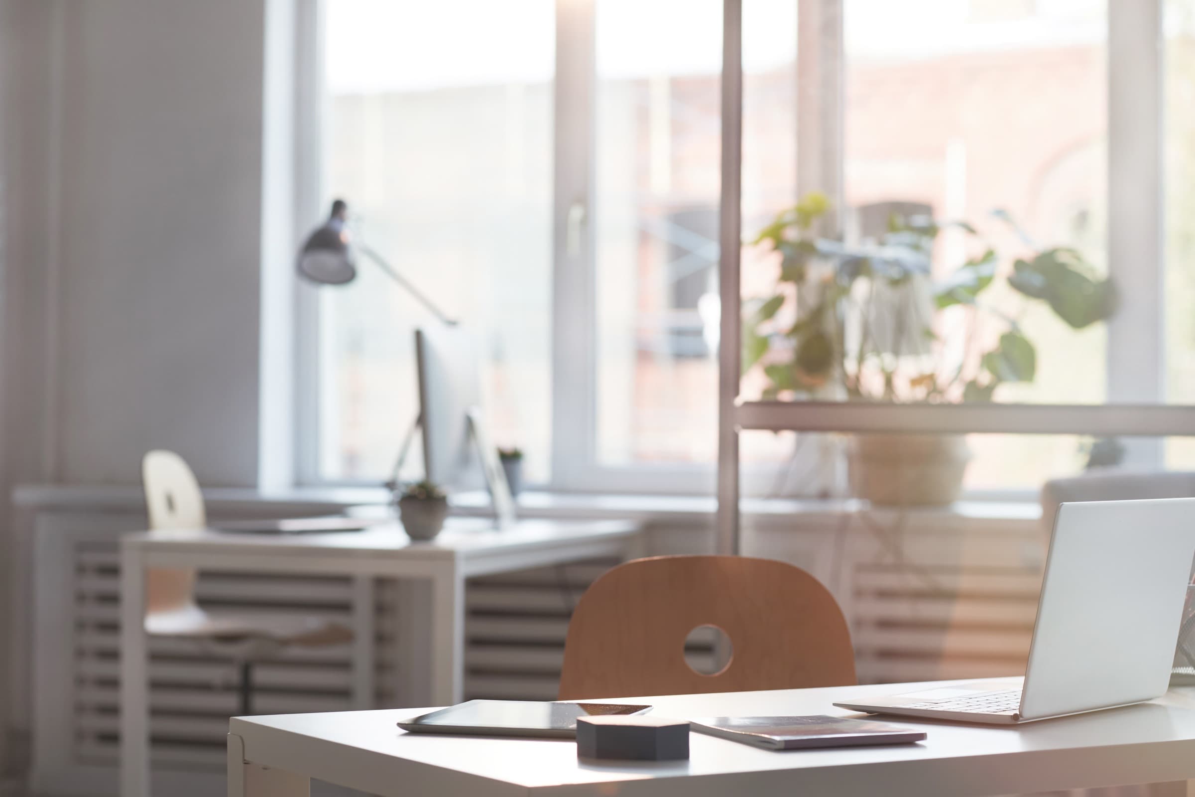 An empty desk and chair in a quiet office filled with soft morning light