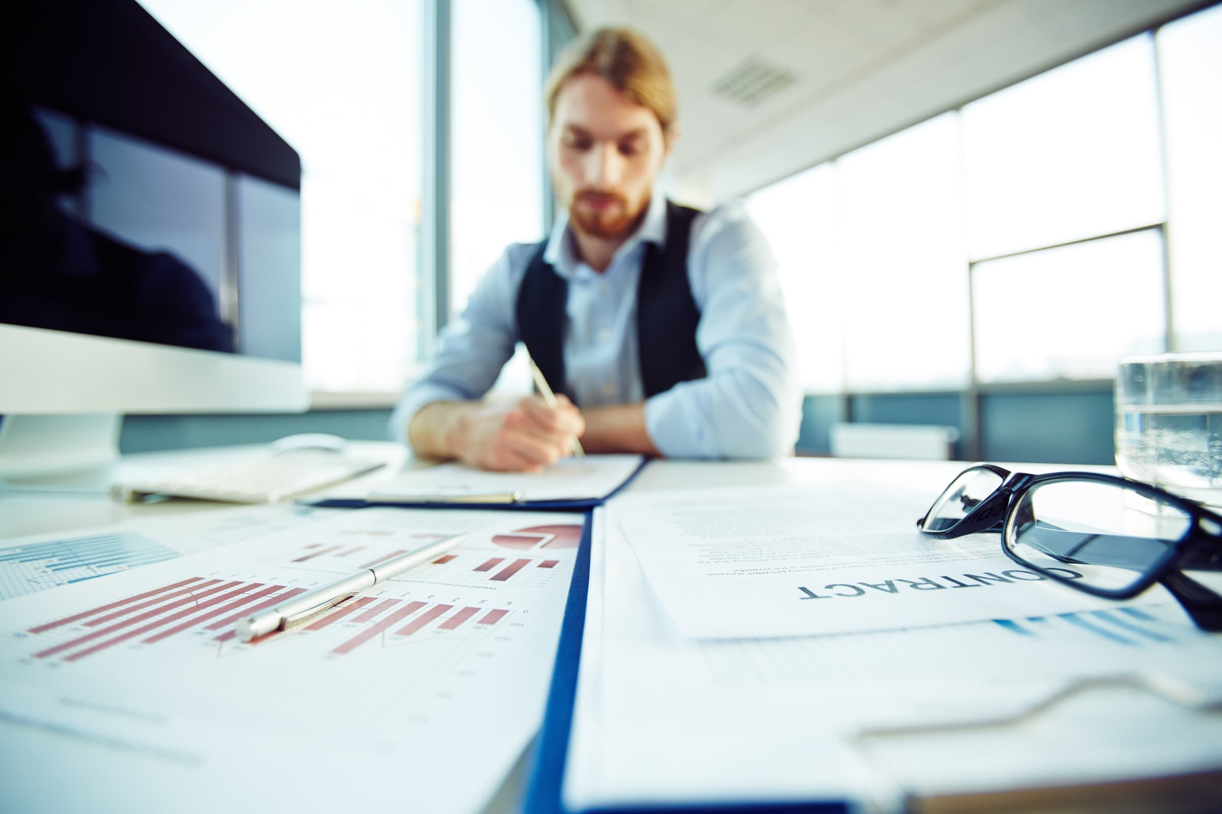 A lawyer at a bright desk working through a contract, reading glasses resting on the papers