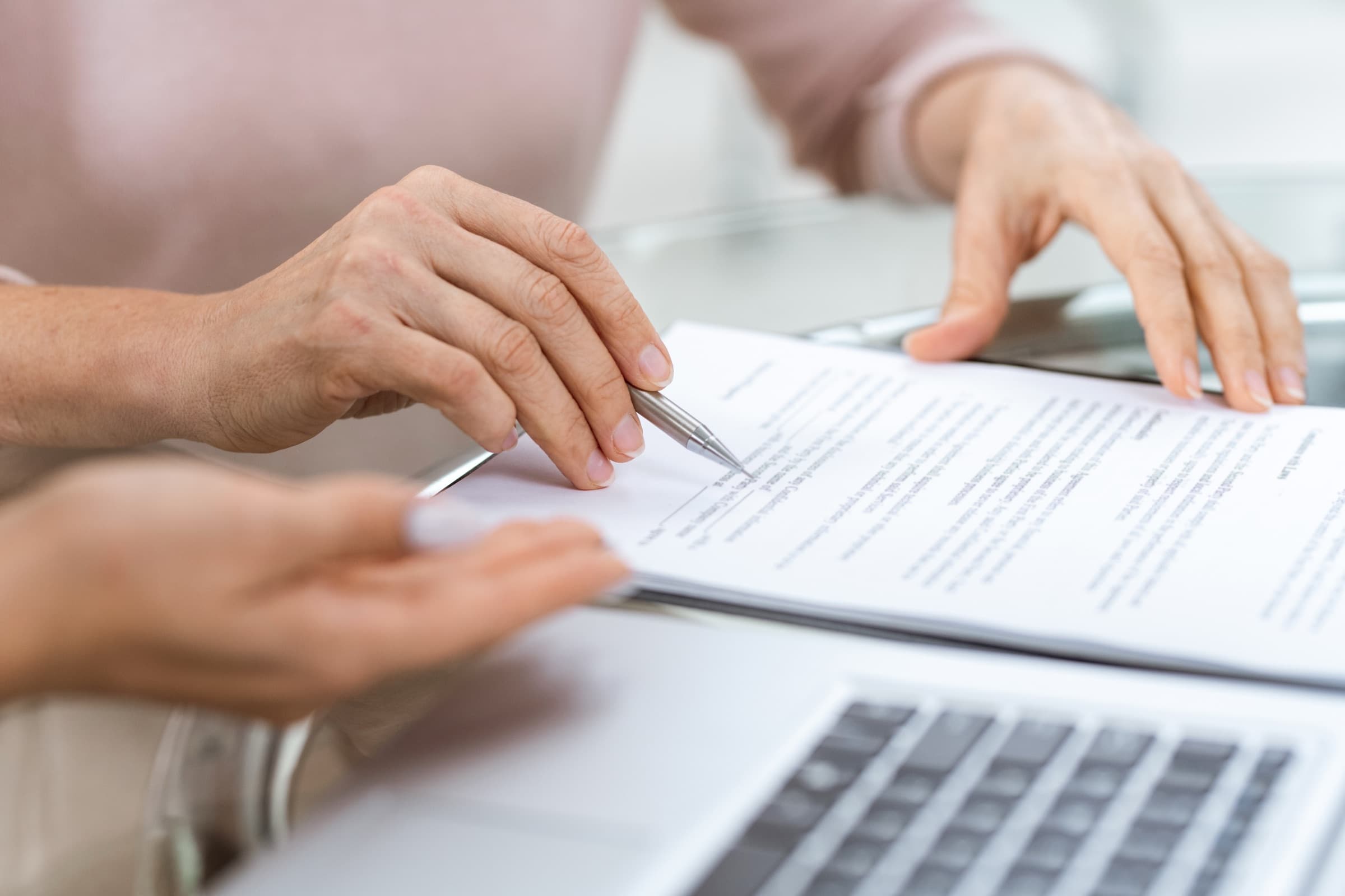A hand with a pen pointing to a specific clause in a printed contract while another person follows along