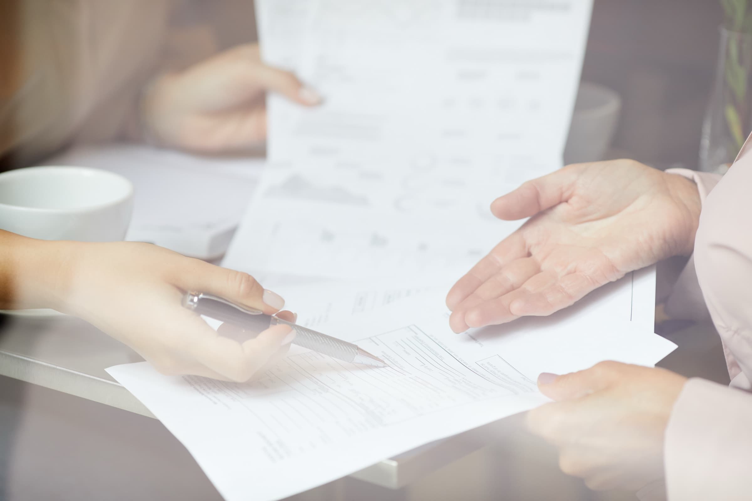Two people passing claim documents across a table, one holding a page of charts
